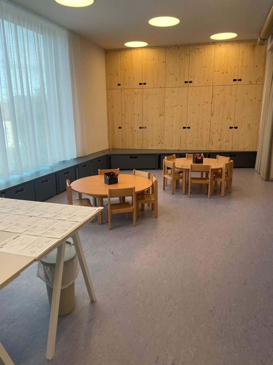 Pracovní koutek s kulatými stolky, kelímky s pastelkami a dřevěnou stěnou skříněk