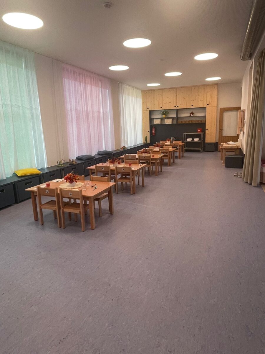 Prostorná jídelna třídy s řadou prostřených stolků a barevnými závěsy